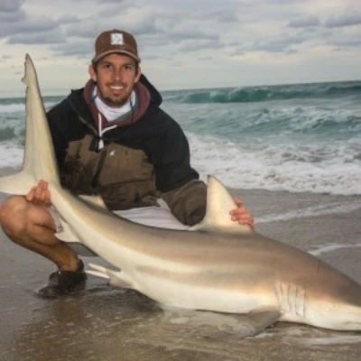 Josh Jorgensen crouching on shore with a shark that he caught
