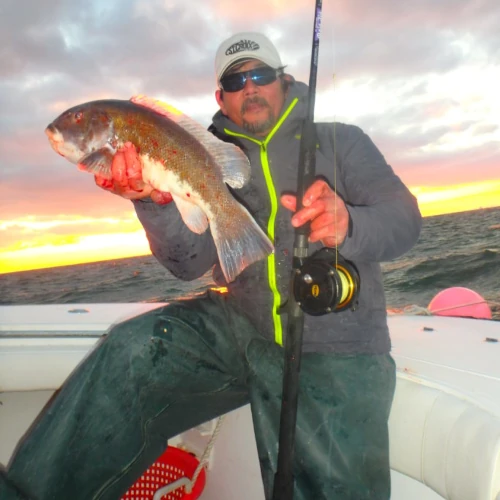 An angler holding a fish and a fishing rod while standing on a boat