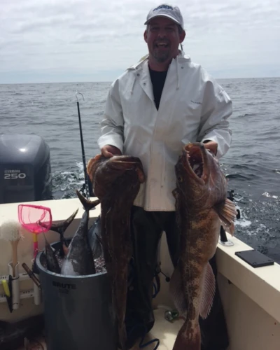 An angler standing on a boat holding two ling fish