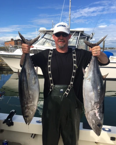 An angler standing on a boat holding two albacore