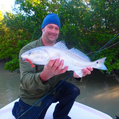 Nick Honachefsky kneeling on a boat holding a whitewashed redfish
