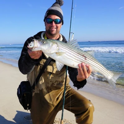 Nick Honachefsky kneeling on the beach holding a striper