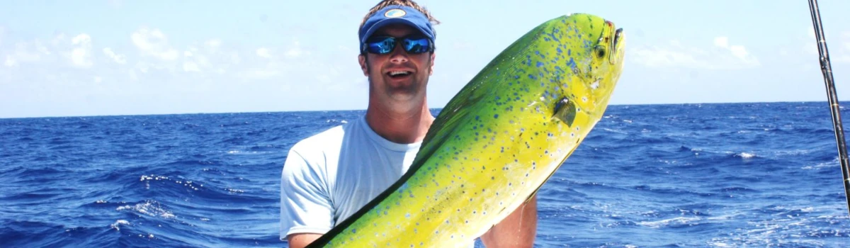 Close-up of Nick Honachefsky standing in front of perfectly blue water holding a mahi