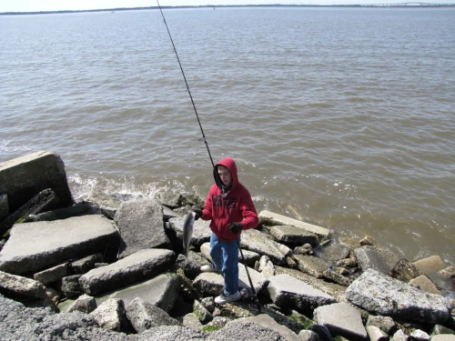 An angler standing on the rocks holding a long fishing rod