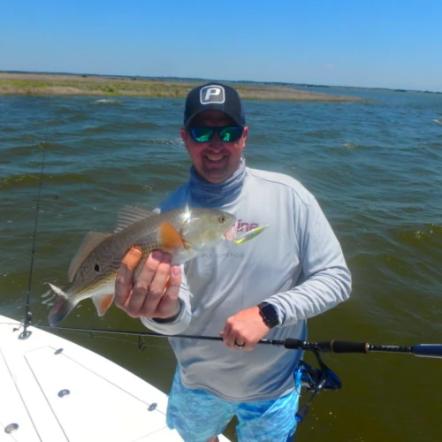 An angler on a boat holding a small redfish