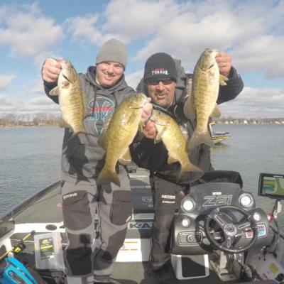 Two anglers on a bass boat holding four bass