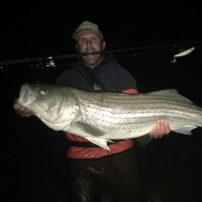 Two anglers in the dark holding striped bass