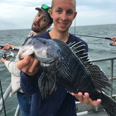 Two anglers on a boat with one fishing and one holding a sea bass