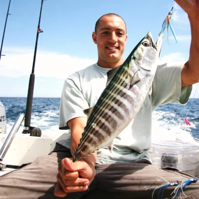 An angler sitting on a boat holding a bonito