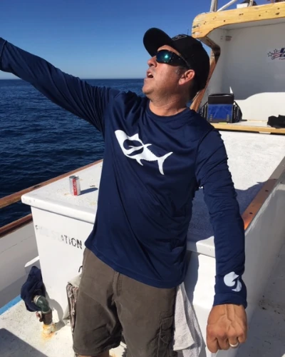 An angler on a boat wearing a TackleDirect long sleeve performance shirt
