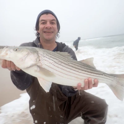 Mickey Melchiondo on a beach holding a striper 