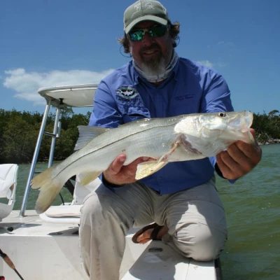 An angler kneeling on a boat holding a snook