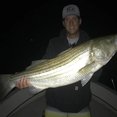 An angler holding a striper while standing on a boat in the dark