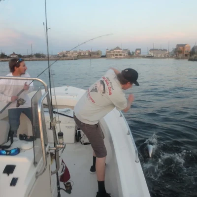 Two men on a boat attempting to pull in a Bluefish