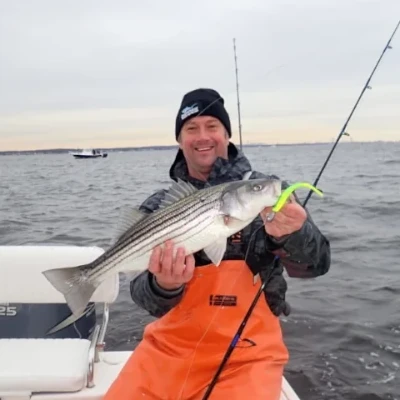 Two men on a boat bring in a landing net with a striped bass fish