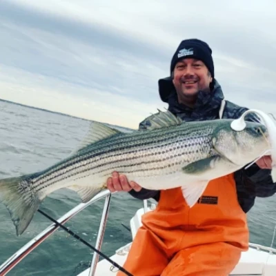 Nick Honachefsky sitting on a boat holding a striped bass with a white jig in its mouth
