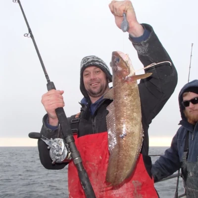 An angler holding a rod and a fish up while another looks on