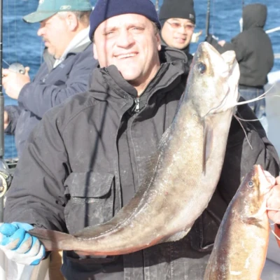An angler holding a fish on a boat with other anglers fishing in the background