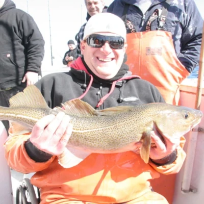 An angler sitting on a boat holding a fish with other anglers in the background
