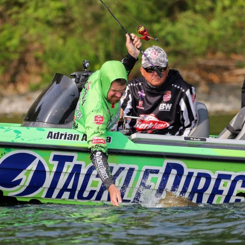 Adrian Avena reaching down from his boat to grab a bass he just caught