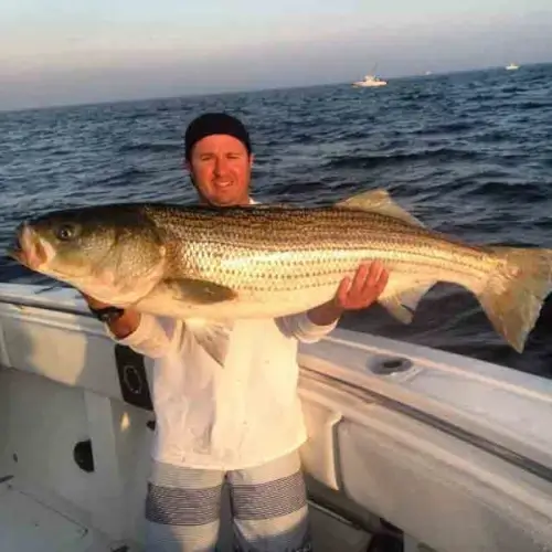 Cole Svenson standing on a boat holding a striped bass